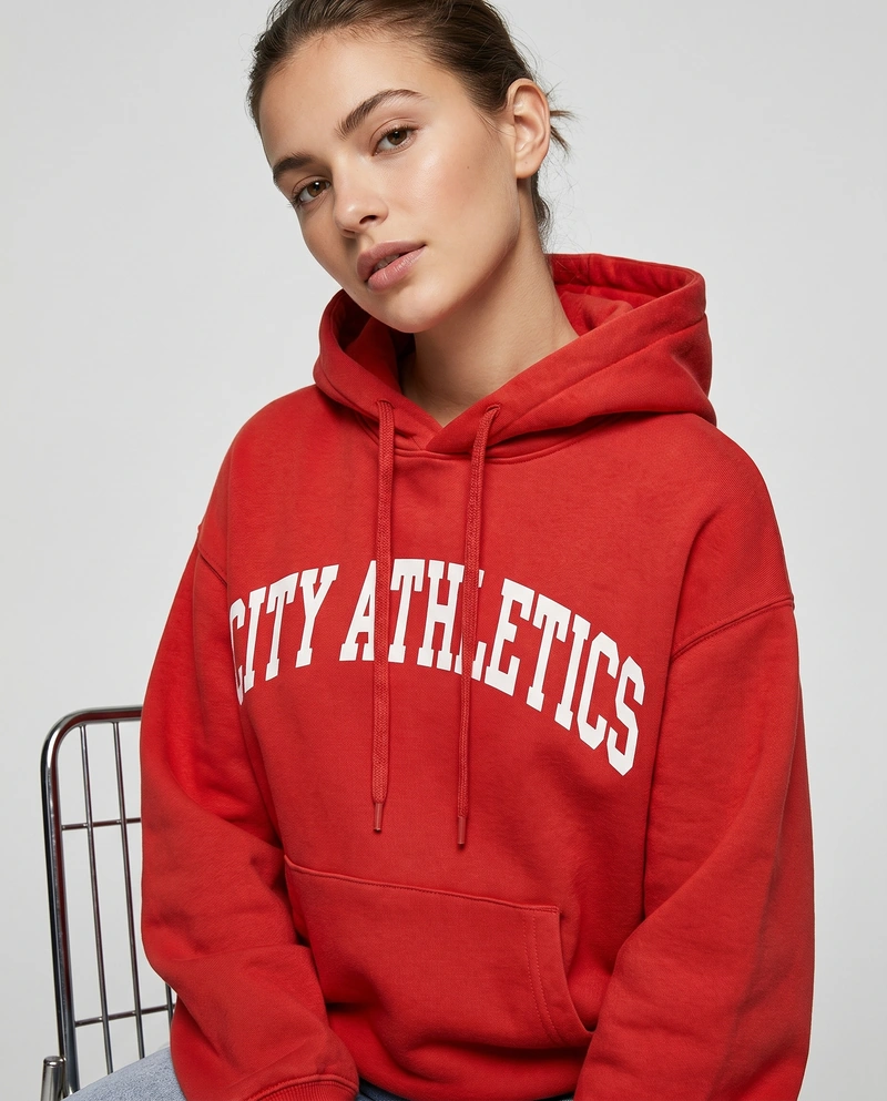 AI-generated: A beautiful 22-year-old female model wearing the @baba (recreateme.ai) hoodie, sitting on a high chair. Studio shoot.
